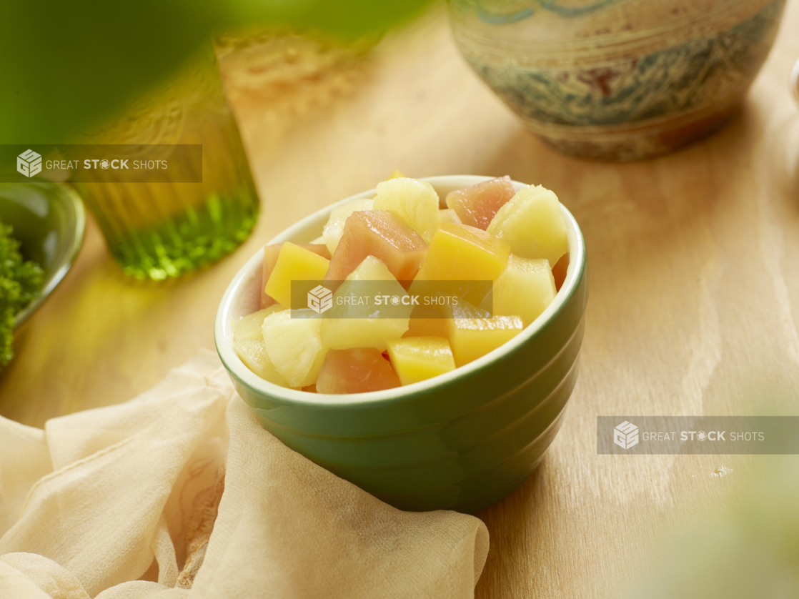 A Green Bowl Filled With a Tropical Fruit Salad of Cut Pineapples, Peaches and Papaya on a Wooden Table in an Indoor Setting