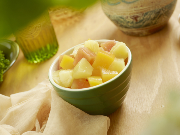 A Green Bowl Filled With a Tropical Fruit Salad of Cut Pineapples, Peaches and Papaya on a Wooden Table in an Indoor Setting