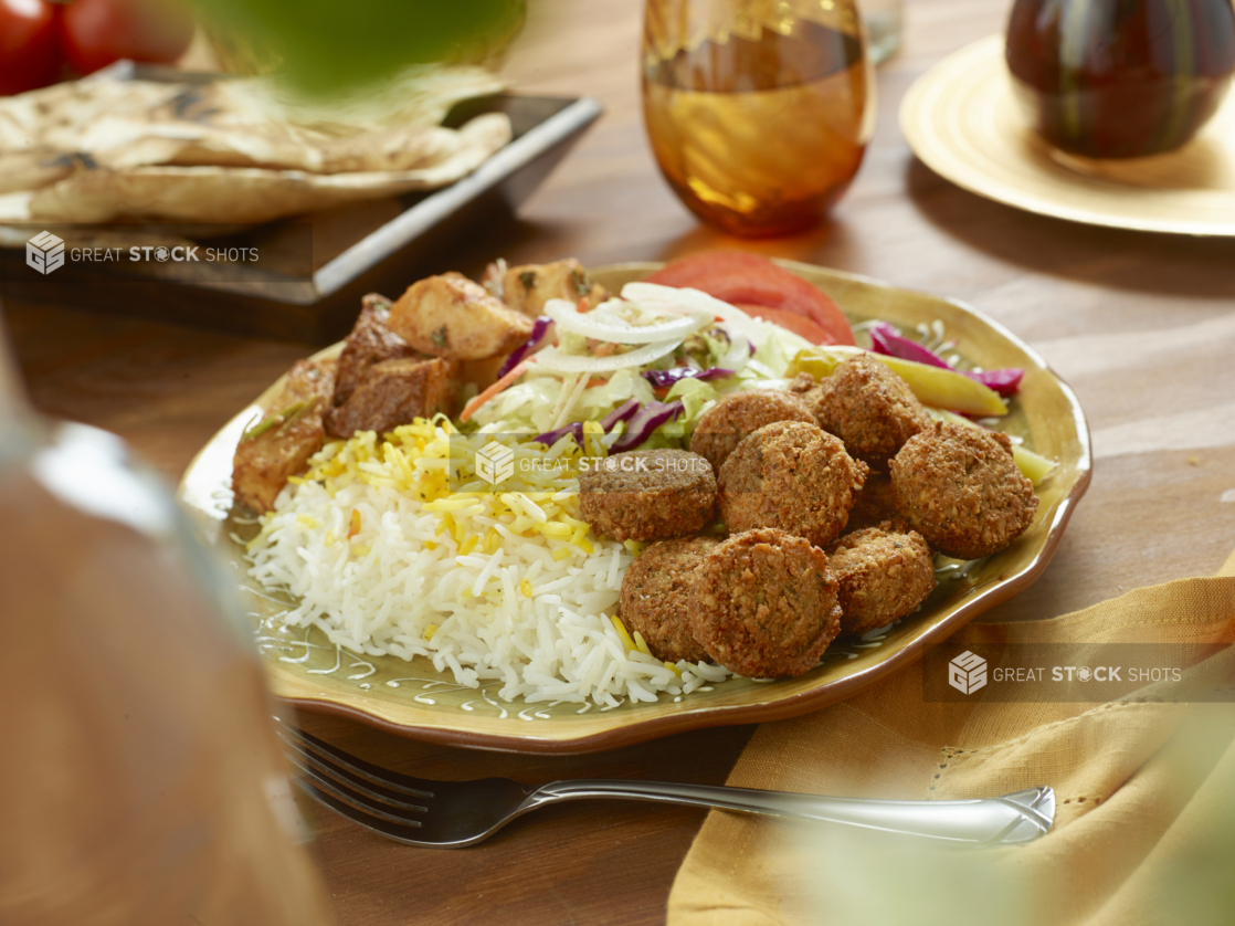 Falafel Combo Dinner with a Garden Salad, Roasted Garlic Potatoes, Picked Veggies and White Rice in a Ceramic Dish on a Wooden Table in an Indoor Setting