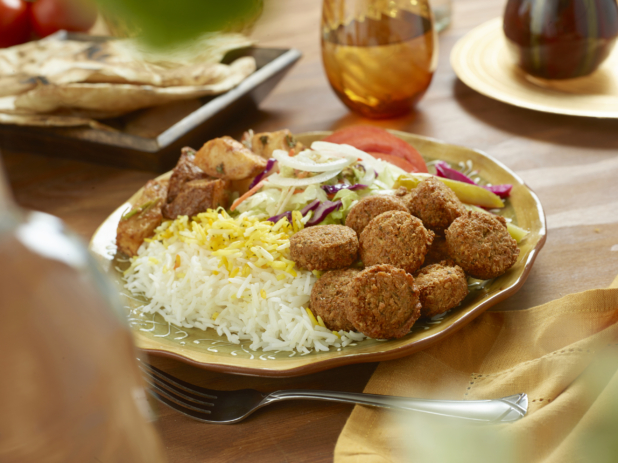 Falafel Combo Dinner with a Garden Salad, Roasted Garlic Potatoes, Picked Veggies and White Rice in a Ceramic Dish on a Wooden Table in an Indoor Setting
