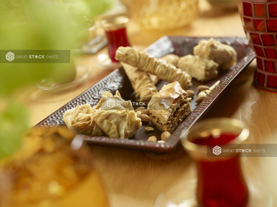 A Brown Rectangular Ceramic Platter with Baklava Pastry in Varying Sizes and Shapes on a Wooden Table in an Indoor Setting