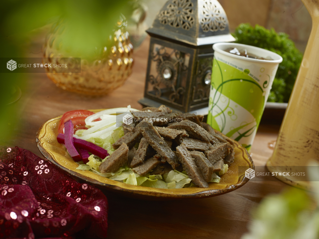 Gyro Salad with Shredded Lettuce, Sliced White Onions, Sliced Tomatoes and Picked Veggies in a Ceramic Dish with a Fountain Soda on a Wooden Table in an Indoor Setting