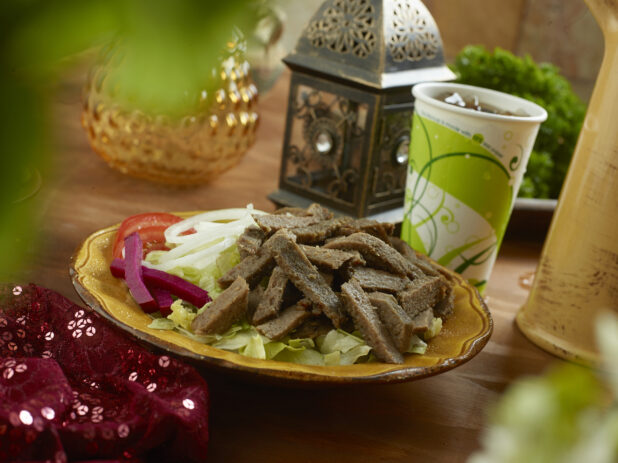 Gyro Salad with Shredded Lettuce, Sliced White Onions, Sliced Tomatoes and Picked Veggies in a Ceramic Dish with a Fountain Soda on a Wooden Table in an Indoor Setting