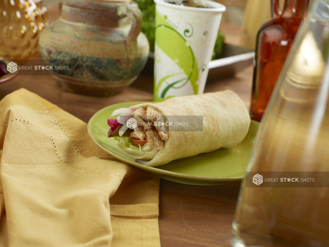 Chicken Souvlaki Pita Wrap with Pickled Veggies and Fresh Vegetables on a Round Ceramic Dish with a Cold Drink on a Wooden Table in an Indoor Setting