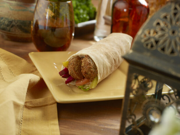 Falafel Pita Wrap with Pickled Veggies and Fresh Vegetables on a Rectangular Ceramic Dish on a Wooden Table in an Indoor Setting