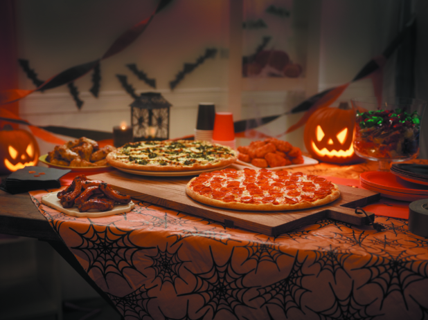 Halloween Pizza Party with Two Pizzas, BBQ Ribs, Chicken Wings and Chicken Nuggets on a Wooden Table in a Decorated Family Room