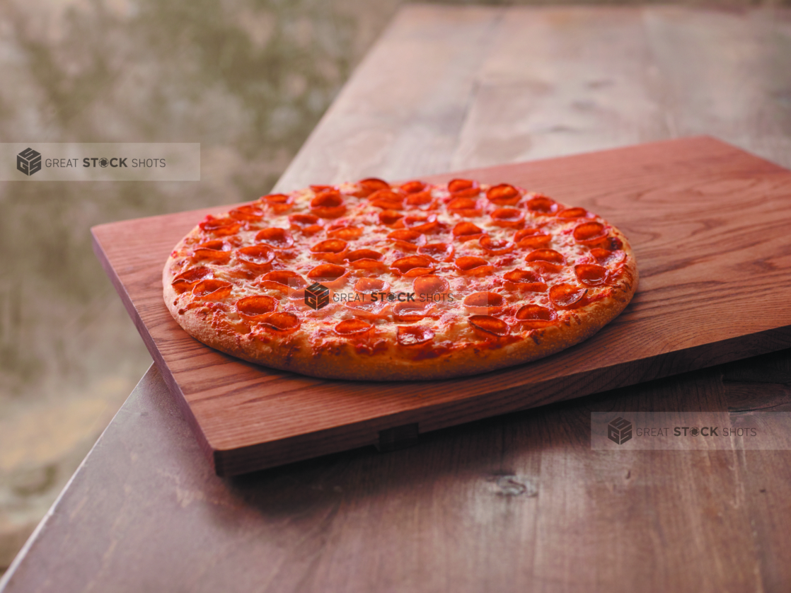 Whole Pepperoni Pizza on a Wooden Cutting Board on a Wooden Table Against a Brown Canvas Background