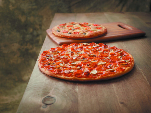 Large Whole Canadian Pizza with Pepperoni, Mushrooms and Bacon Toppings on a Wooden Table with a Tomato and Olive Focaccia Bread against a Brown Canvas Background