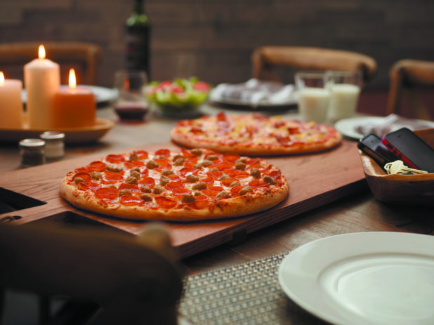 A Family Pizza Dinner Setting with Two Pizzas, a Garden Salad and Red Wine on a Large Wooden Table with Table Settings in a Family Dining Room