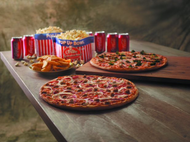 Movie Night Special with Two 3-Topping Pizzas, Microwave Popcorn, Potato Wedges and Cans of Coca-Cola on a Wooden Table Against a Brown Canvas Background