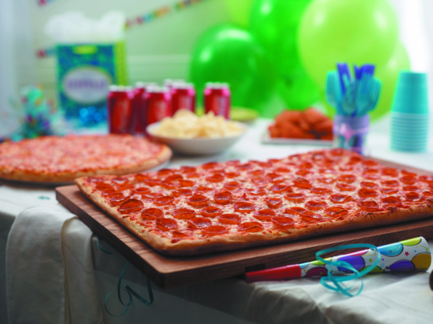 Birthday Pizza Party with Party-sized Pepperoni Pizza, Cheese Pizza, BBQ Chicken Wings, Potato Chips and a 6-pack of Soda with Party Decorations in a Bright Indoor Family Room