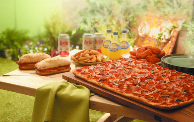 A Pizza Party with a Large Sicilian Pizza, Boneless Wings, Potato Wedges, Italian Sandwiches and Cold Drinks on a Picnic Table in an Outdoor Garden Setting
