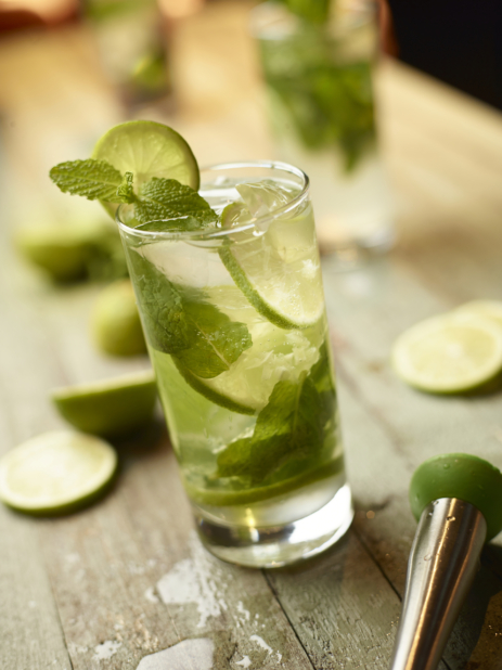 Close Up of a Mojito Cocktail with Fresh Lime Slices and Fresh Mint Leaves on an Aged Wooden Surface