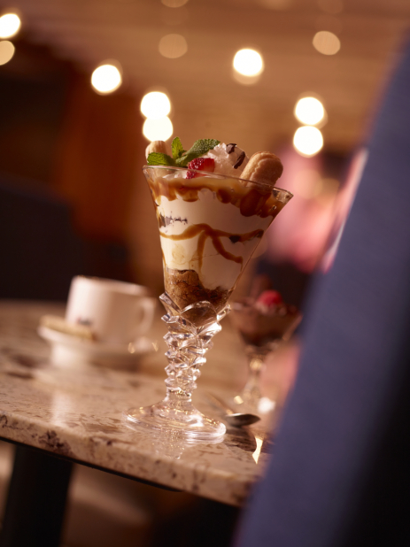 Mini Parfait in Glass Cup with Whipped Cream, Lady Fingers, Caramel and Ice Cream on a Marble Surface in an Indoor Restaurant Setting