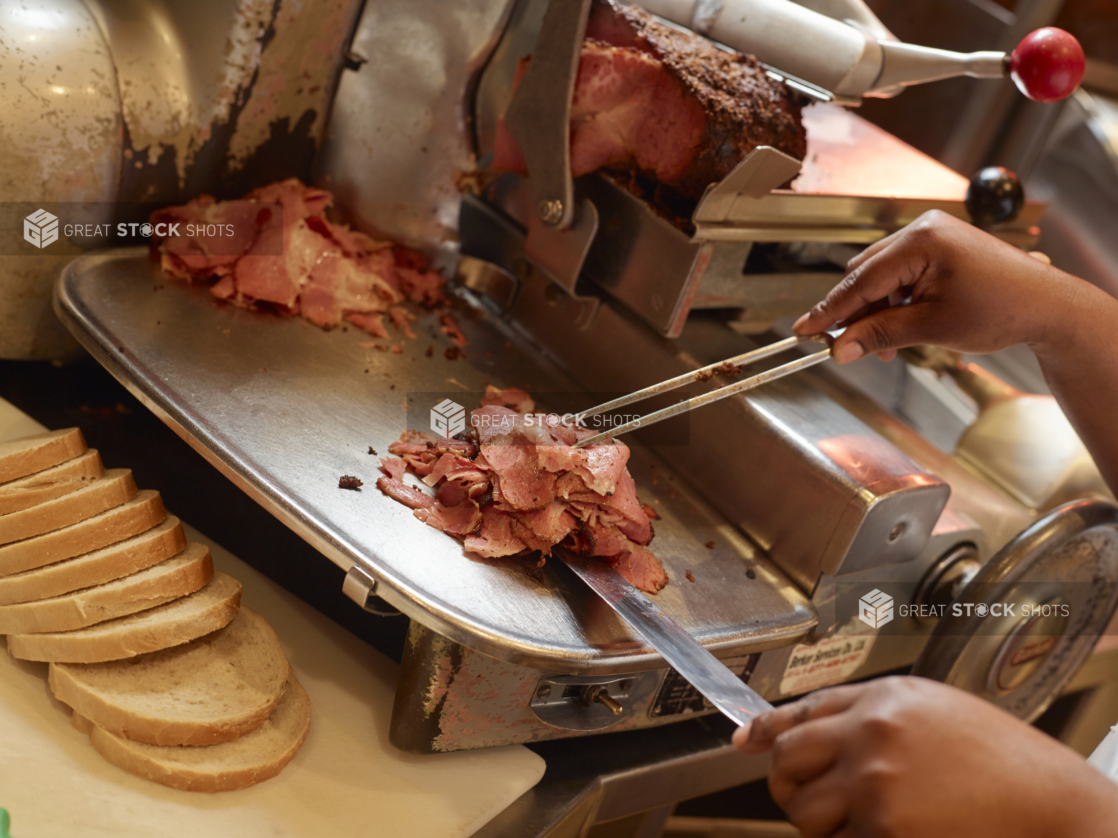 Chefs Hands Carving Pastrami Slices in a Restaurant Kitchen Resting with a Loaf of Sliced White Rye Bread