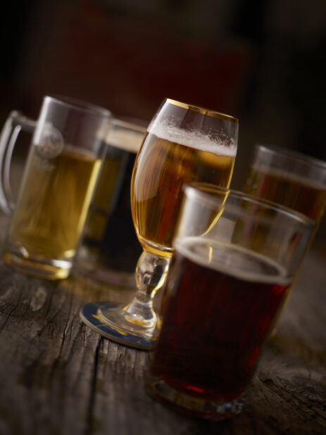 Assorted Glasses of Beer, Lager and Stout on an Aged Wooden Table Against a Dark Brown Background