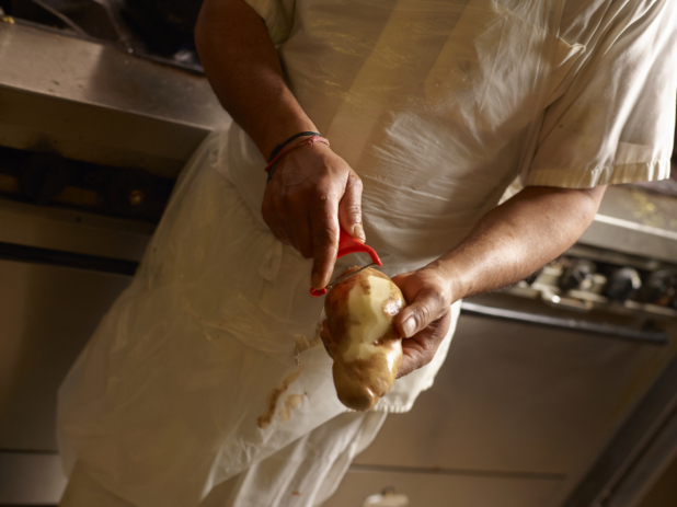 Chef Peeling a Large Potato with a Red Vegetable Peeler in a Restaurant Kitchen Setting