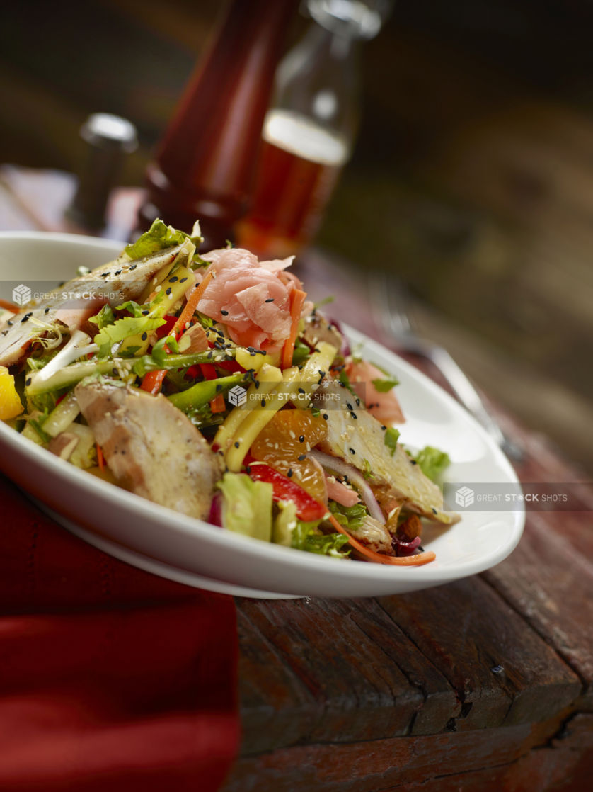 Grilled Chicken, Fresh Fruit and Chopped Vegetable Meal Salad with Black Sesame and Asian Salad Dressing on an Old Aged Painted Wood Table in a Restaurant Setting