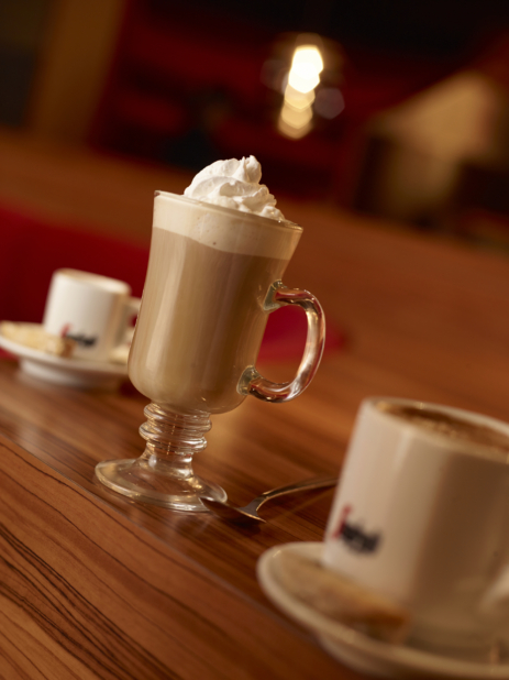 Close Up of a Cold Latte with Whipped Cream Flanked by Segafredo Espresso Cups and Sauces on a Wooden Tablecold latt