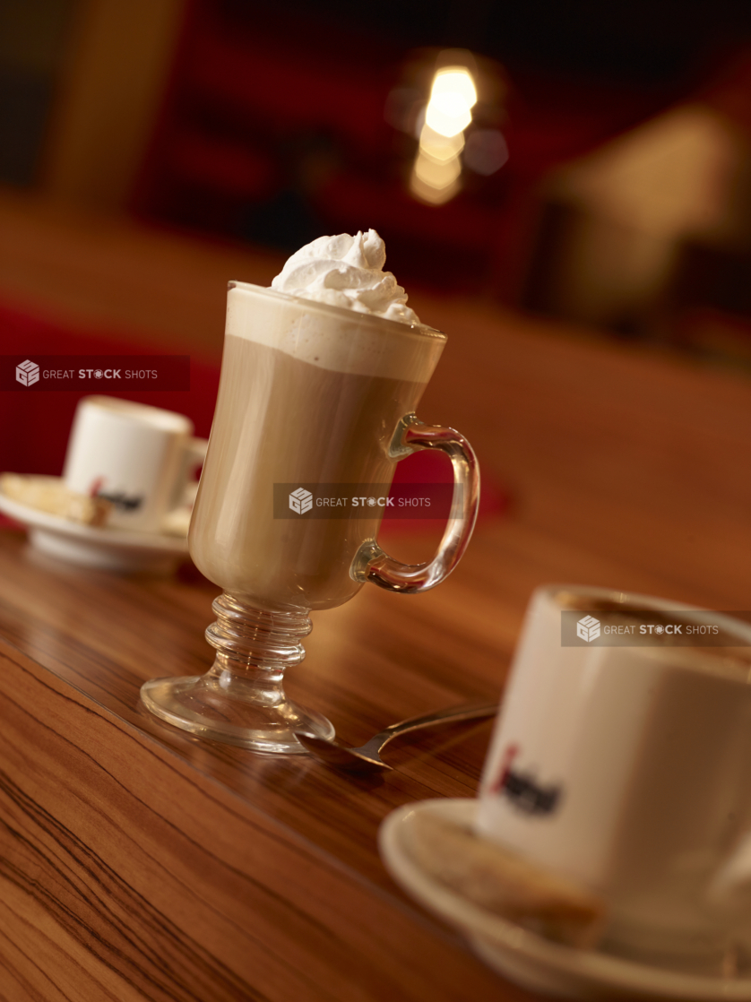 Close Up of a Cold Latte with Whipped Cream Flanked by Segafredo Espresso Cups and Sauces on a Wooden Tablecold latt