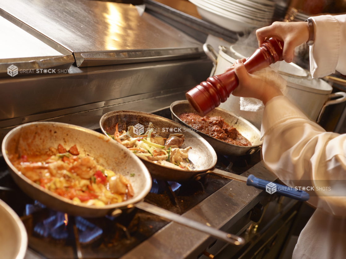 Chef Adding Freshly Ground Black Pepper into Seafood Sauté Cooking Over a Gas Stove in an Indoor Kitchen Setting