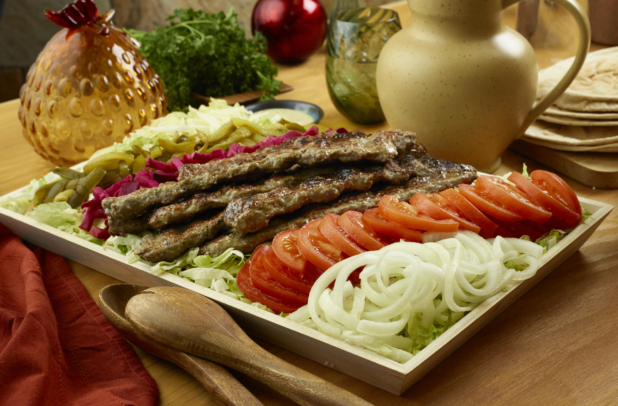 Kebab platter with tomatoes, onion, and pickles on a bed of shredded lettuce on a wood catering tray, wood tabletop, aesthetic objects surrounding