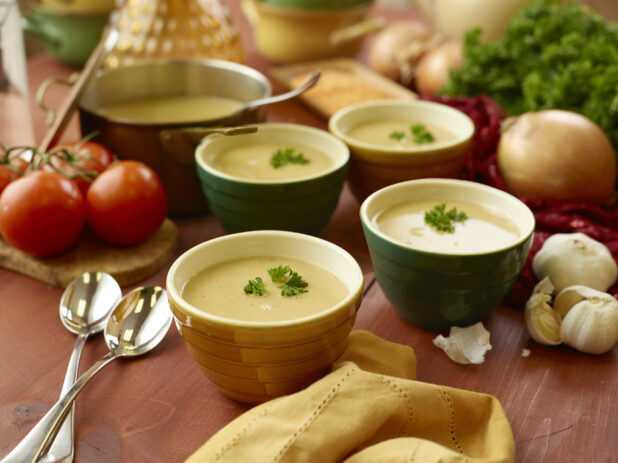 Four Ceramic Bowls of Vegetarian Lentil Soup with Fresh Parsley Garlic on a Wooden Table with Fresh Ingredients in an Indoor Setting