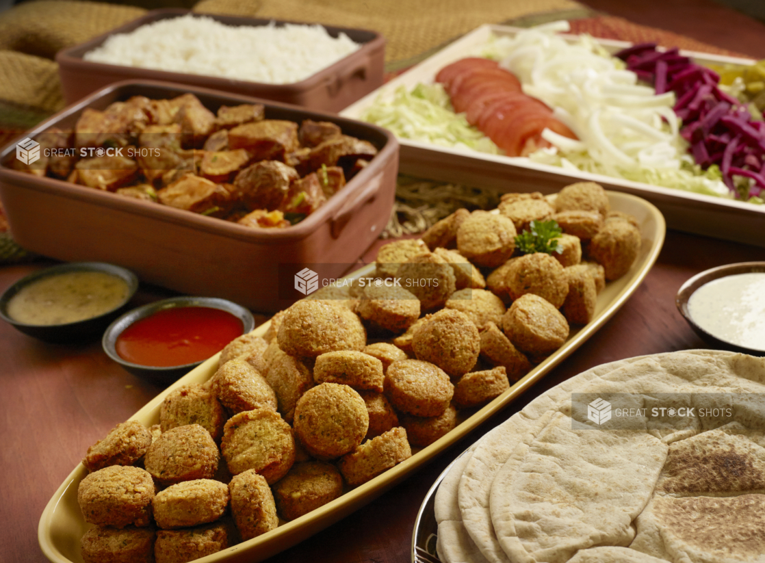 Build Your Own Falafel Pita Wrap Family Meal Combo with Ingredients and Side Dishes of Rice and Garlic Potatoes on a Wooden Table in an Indoor Setting - Variation