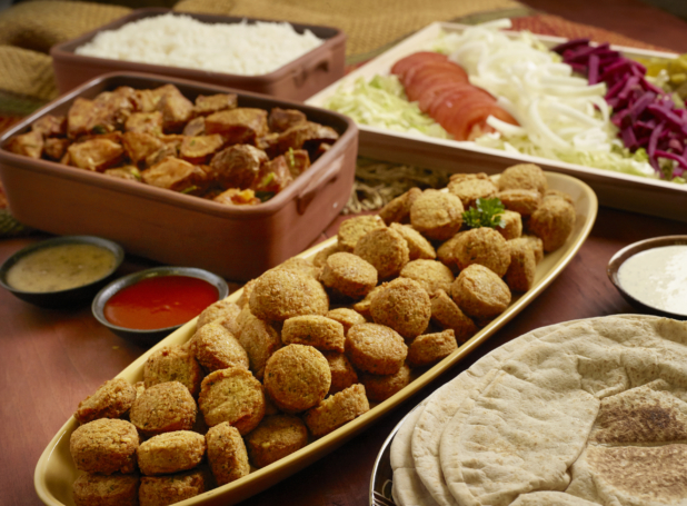 Build Your Own Falafel Pita Wrap Family Meal Combo with Ingredients and Side Dishes of Rice and Garlic Potatoes on a Wooden Table in an Indoor Setting - Variation