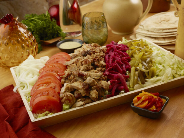 Large Rectangular Wood Serving Tray of Chicken Shawarma Salad with Toppings and Ingredients with Pita Bread on a Wooden Table Surface in an Indoor Setting