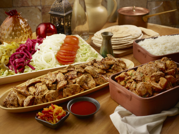 Build Your Own Marinated Chicken Pita Wrap Family Meal Combo with Ingredients and Side Dishes of Rice and Garlic Potatoes on a Wooden Table in an Indoor Setting