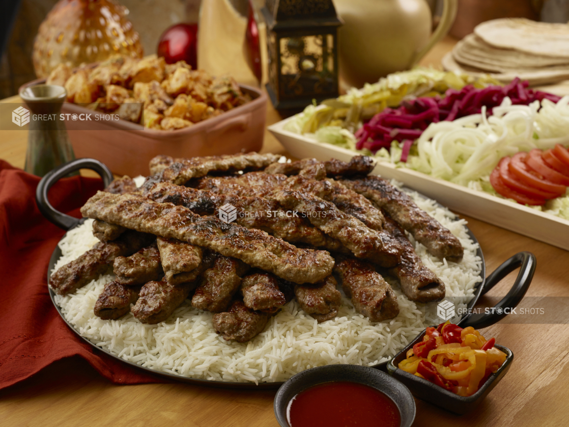 Build Your Own Beef Kebab Pita Wrap Family Meal Combo with Beef Kebab on a Bed of White Rice and a Side of Garlic Potatoes on a Wooden Table in an Indoor Setting