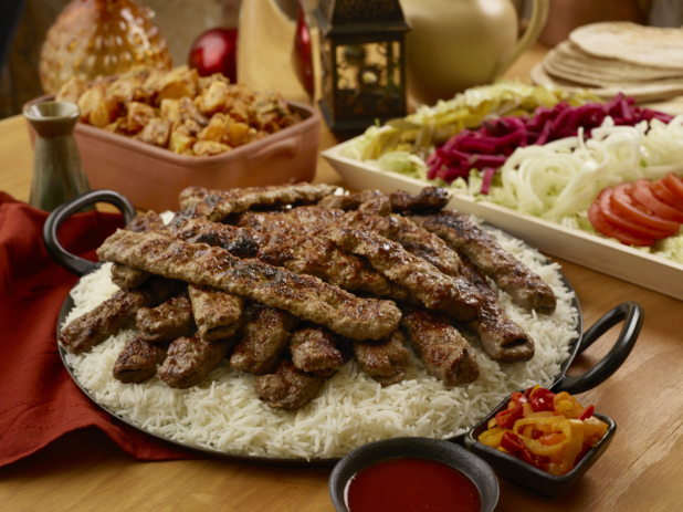 Build Your Own Beef Kebab Pita Wrap Family Meal Combo with Beef Kebab on a Bed of White Rice and a Side of Garlic Potatoes on a Wooden Table in an Indoor Setting