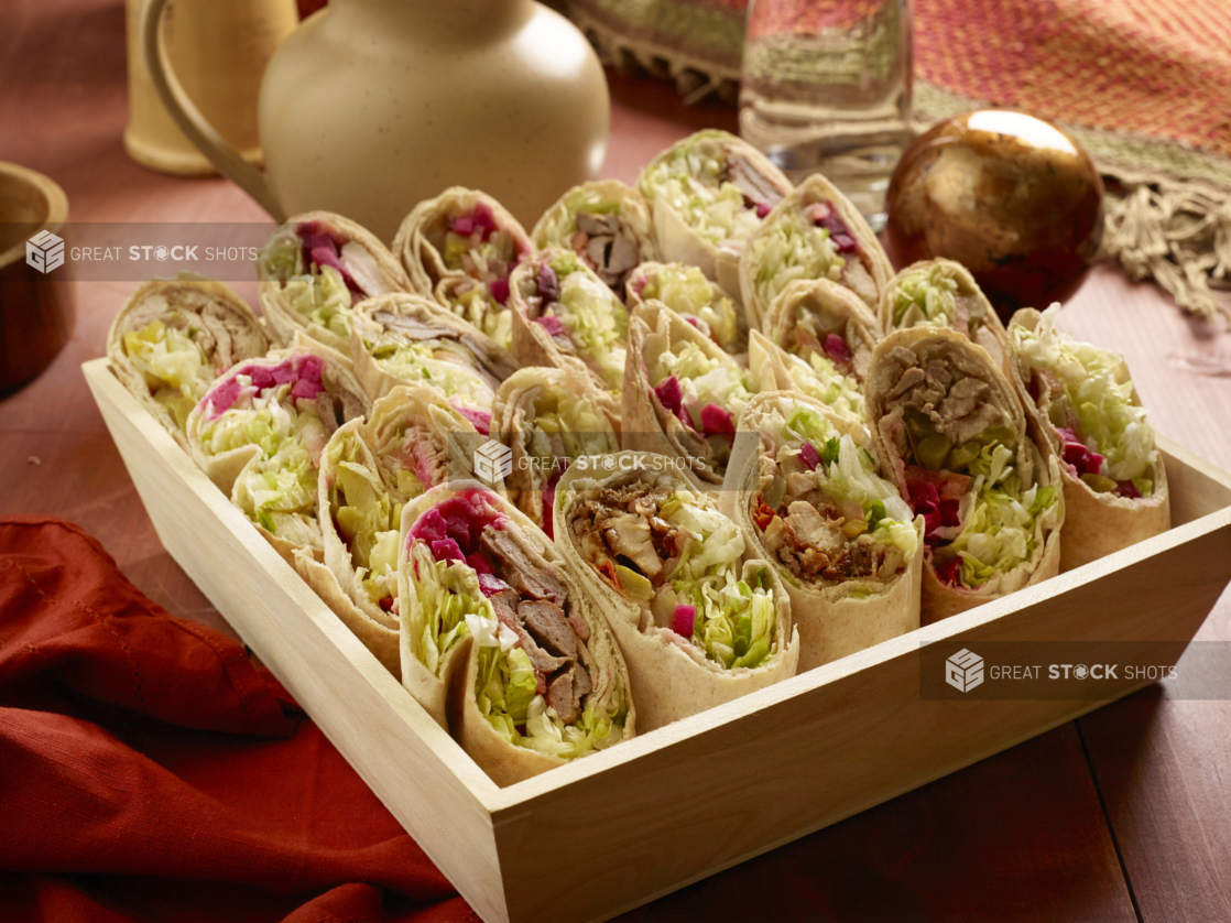 Assorted Middle Eastern Pita Wraps (Chicken and Beef Shawarma, Chicken and Beef Kebabs) in a Deep Square Wood Serving Tray for Catering on a Wooden Table in an Indoor Setting