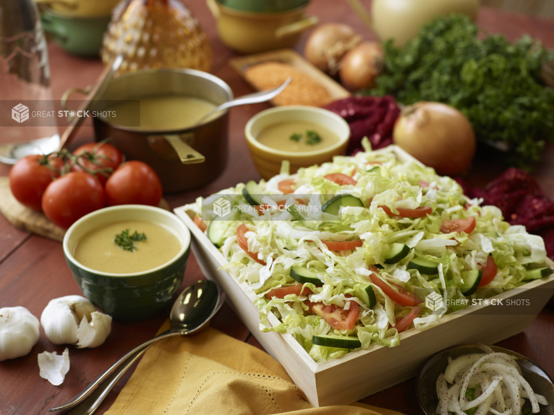 Wooden Serving Tray of Fresh Garden Salad for Catering with Bowls of Lentil Soup and Raw Ingredients on a Wooden Table in an Indoor Setting