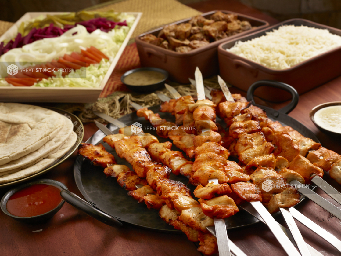 Build Your Own Chicken Kebab Pita Wrap Family Meal Combo with Ingredients and Side Dishes of Rice and Garlic Potatoes on a Wooden Table in an Indoor Setting