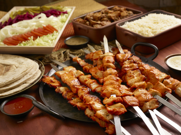 Build Your Own Chicken Kebab Pita Wrap Family Meal Combo with Ingredients and Side Dishes of Rice and Garlic Potatoes on a Wooden Table in an Indoor Setting