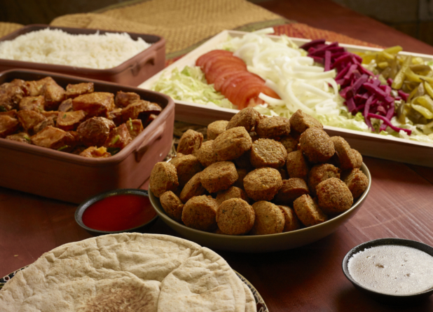 Build Your Own Falafel Pita Wrap Family Meal Combo with Ingredients and Side Dishes of Rice and Garlic Potatoes on a Wooden Table in an Indoor Setting