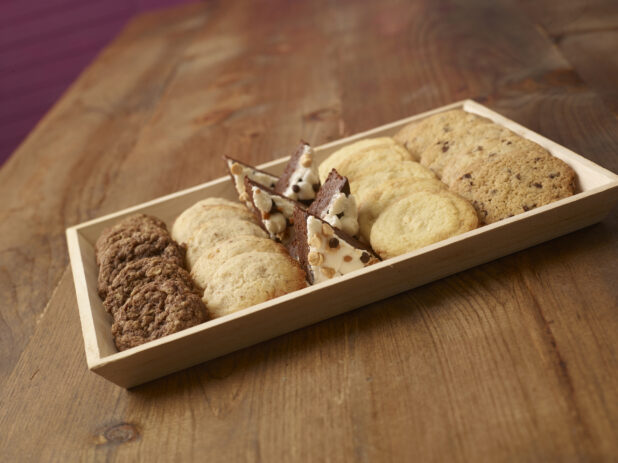 Assortment of cookies and halved dessert squares on a wood catering tray