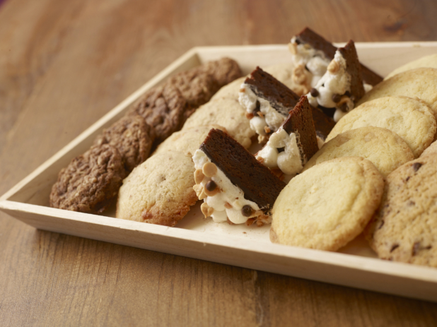 Assortment of cookies and halved dessert squares on a wood catering tray, close-up