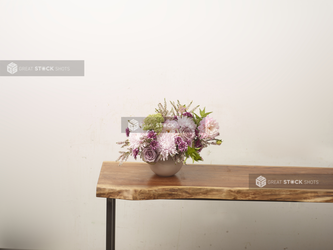 Pink flower arrangement with chrysanthemums and roses in a white vase positioned at the end of a long wooden table