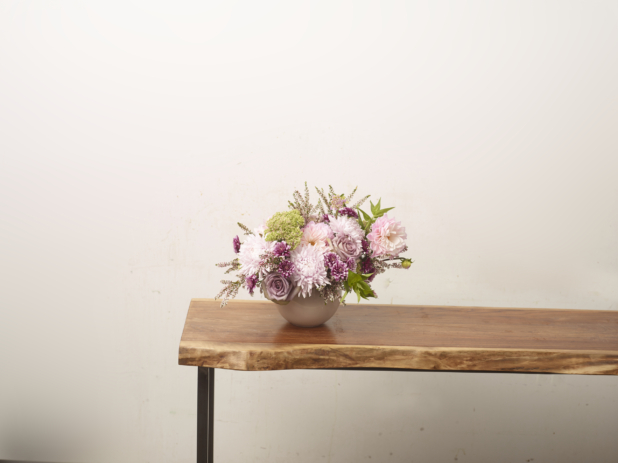 Pink flower arrangement with chrysanthemums and roses in a white vase positioned at the end of a long wooden table