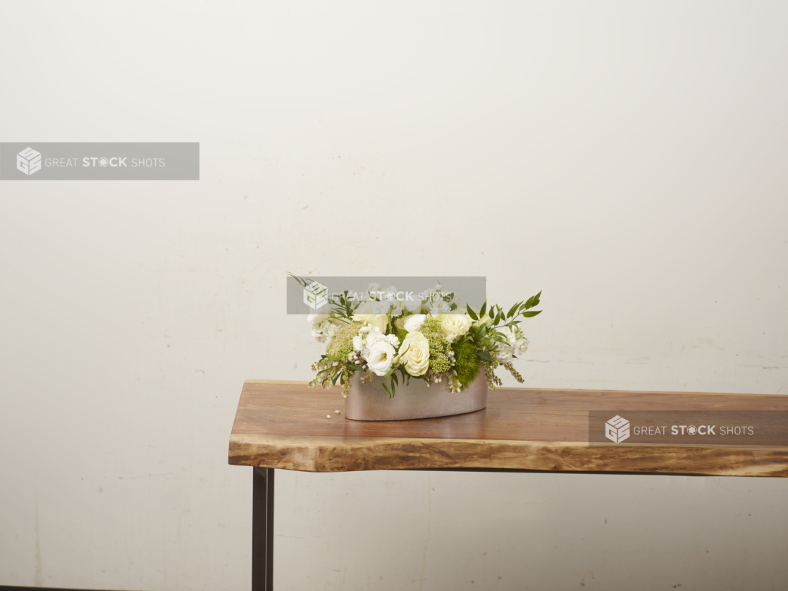 Yellow and white flower arrangement with roses and ranunculus in a white vase positioned at the end of a long wooden table