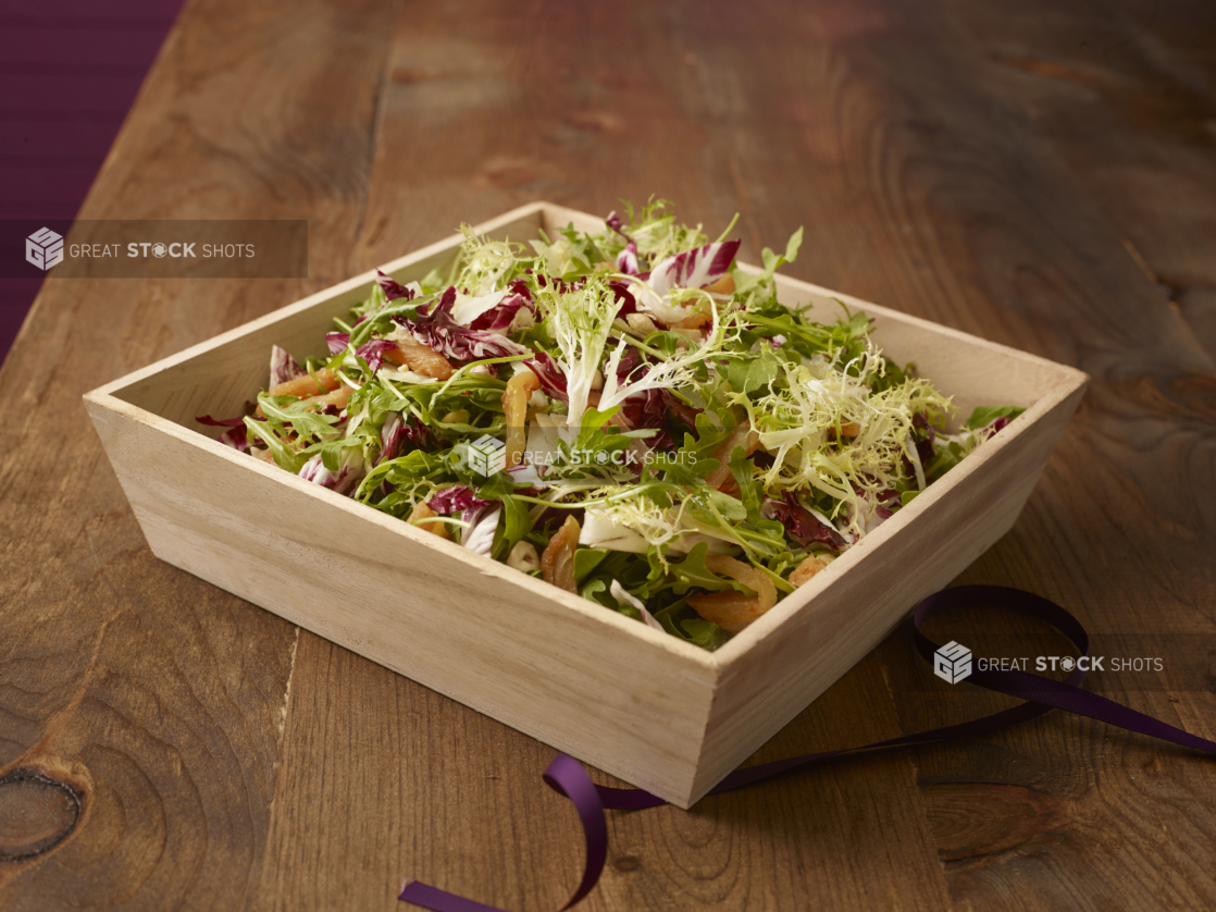 Spring mix salad with roasted yellow peppers in a wood catering box on a wood background, close-up