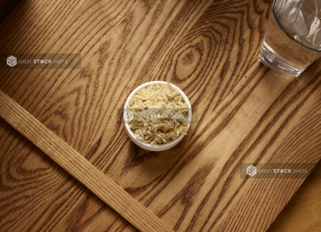 Overhead View of a Small White Ceramic Dish of Kid-Sized Brown Rice Side Dish on a Wooden Cutting Board in an Indoor Setting