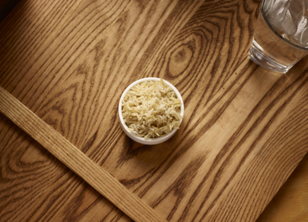 Overhead View of a Small White Ceramic Dish of Kid-Sized Brown Rice Side Dish on a Wooden Cutting Board in an Indoor Setting