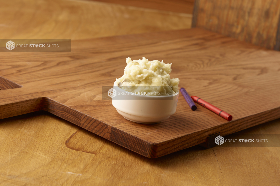 Small White Ceramic Dish of Kid-Sized Mashed Potatoes Side Dish on a Wooden Cutting Board in an Indoor Setting