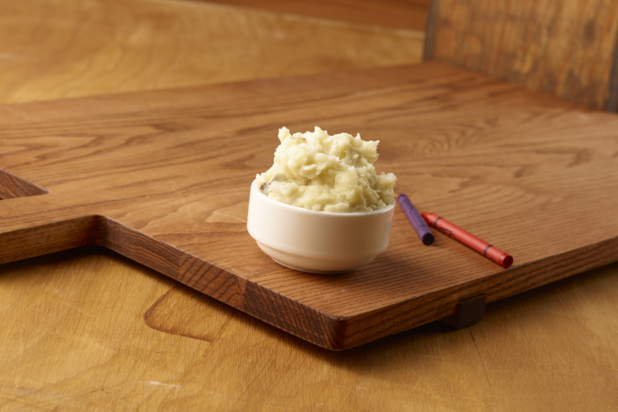 Small White Ceramic Dish of Kid-Sized Mashed Potatoes Side Dish on a Wooden Cutting Board in an Indoor Setting