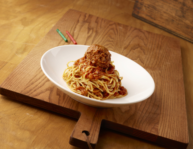 Kids Spaghetti and Meatball in a Large White Ceramic Bowl on a Wooden Cutting Board in an Indoor Setting