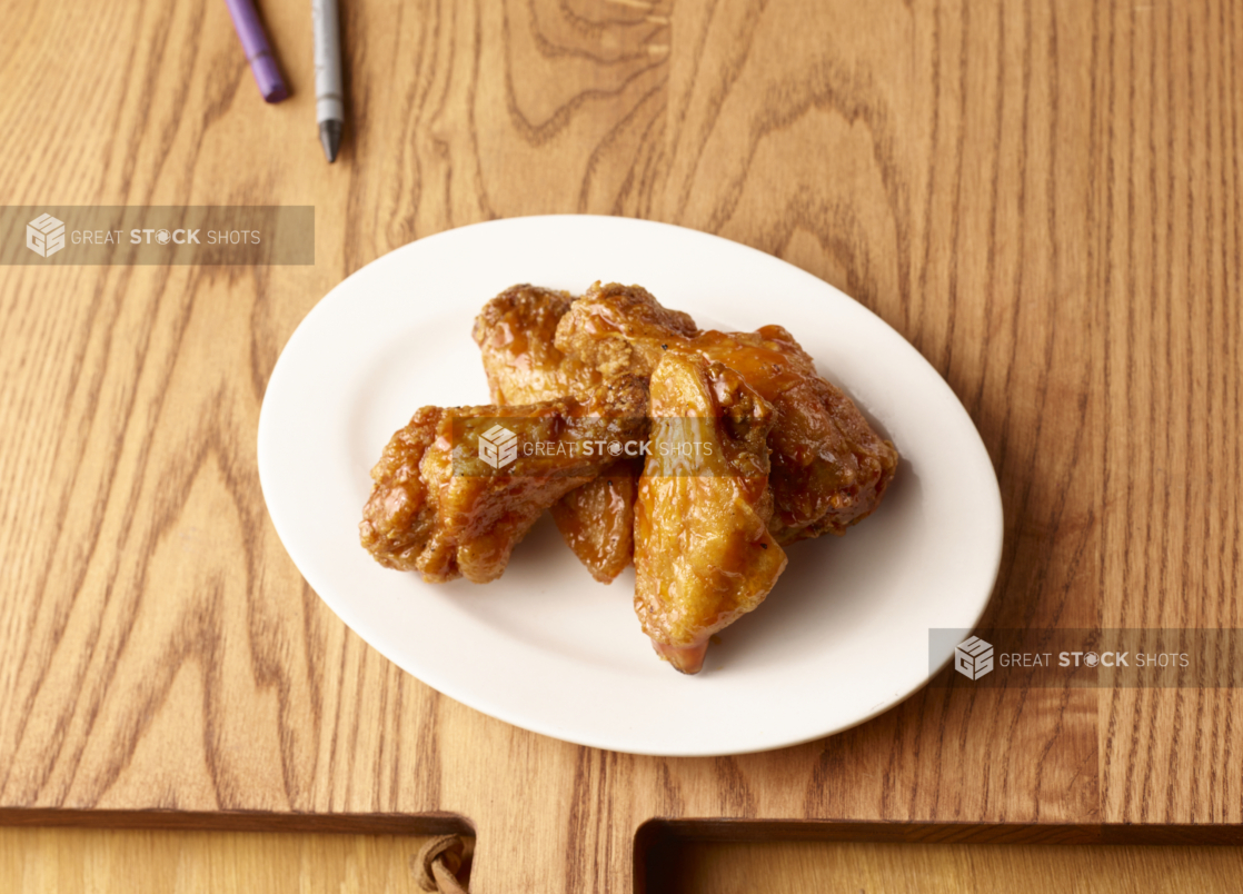 Jumbo Sauced Chicken Wings on a Round White Plate, Close Up on a Wooden Cutting Board with Crayons for Kids